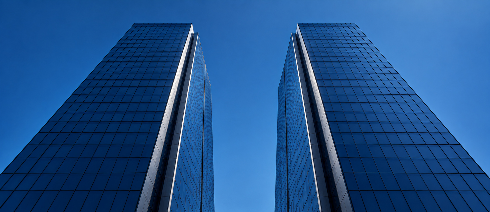 Duas torres corporativas de vidro vistas de baixo contra o céu azul